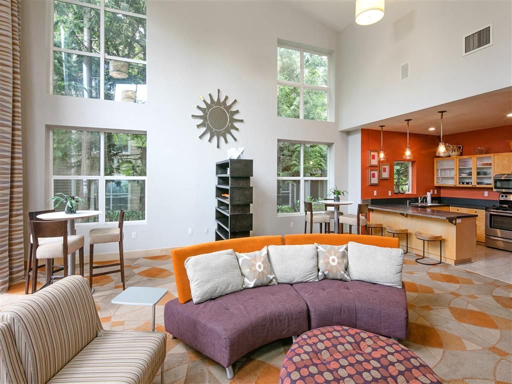 Bright resident lounge with large windows, a purple sectional sofa, and a kitchen island.