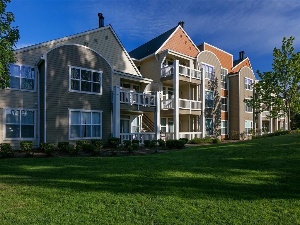 Exterior view of a multi-story apartment building with balconies and green lawn.
