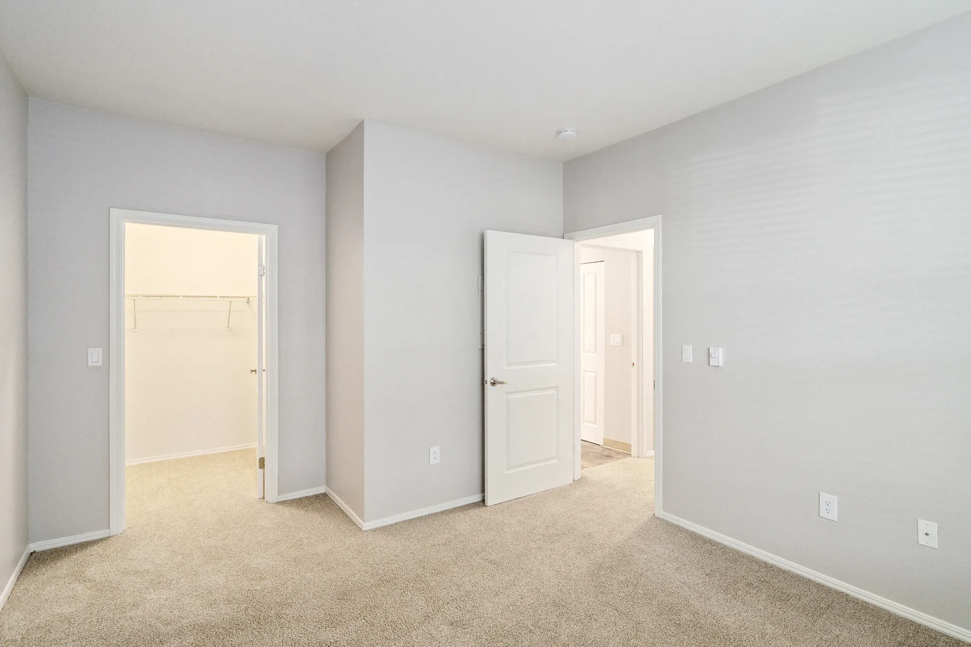 Bedroom interior with beige carpet, light gray walls, and a closet with shelves.