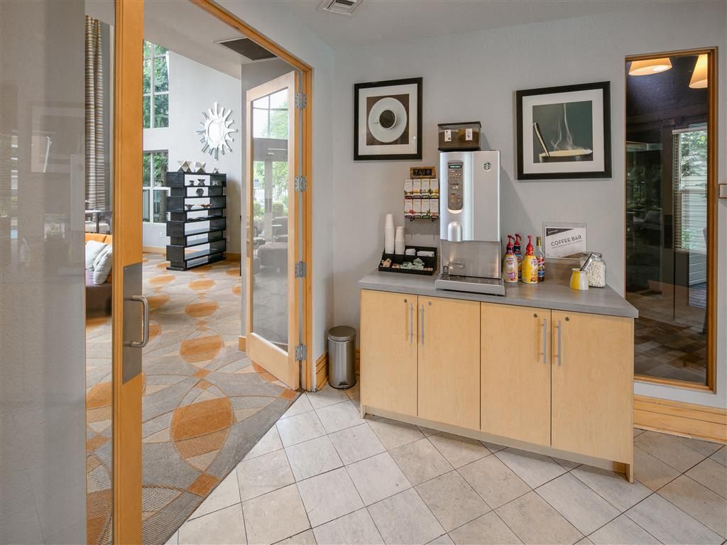 Coffee station in a modern apartment community lobby with a beverage dispenser and framed art.