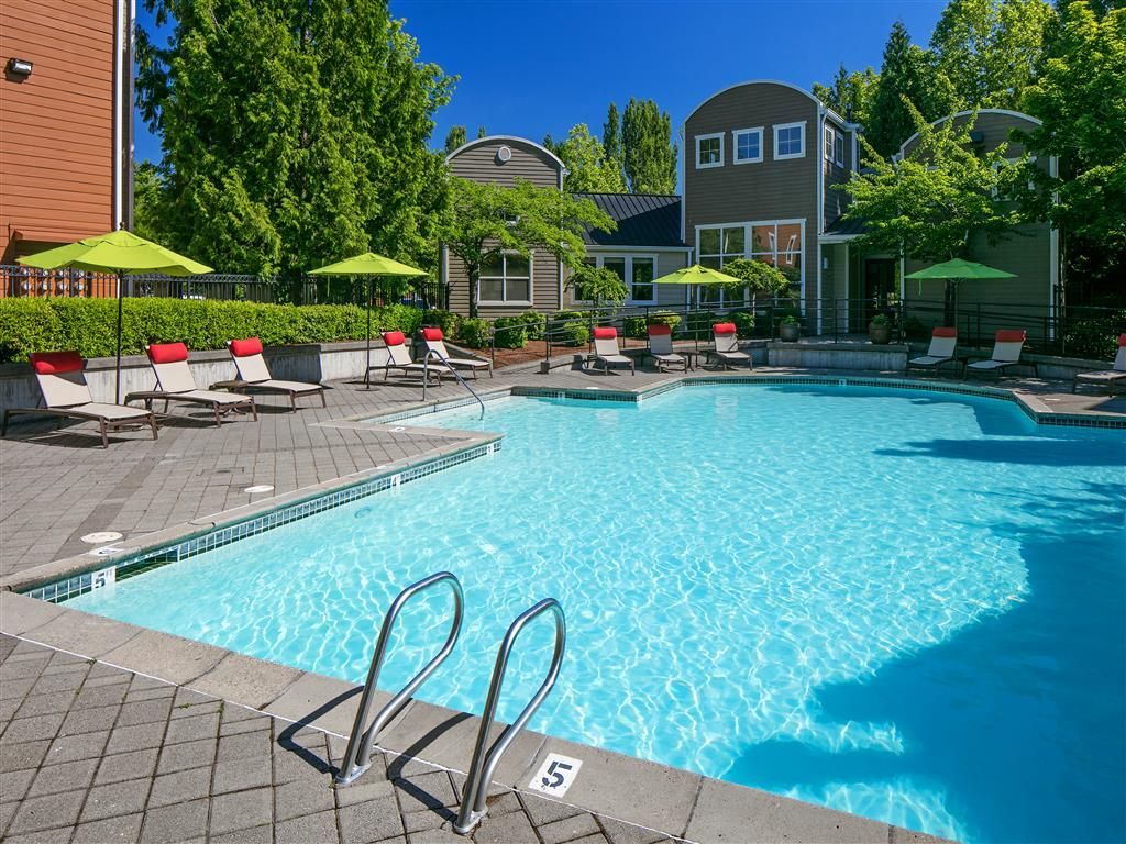Outdoor community pool with lounge chairs and green umbrellas.