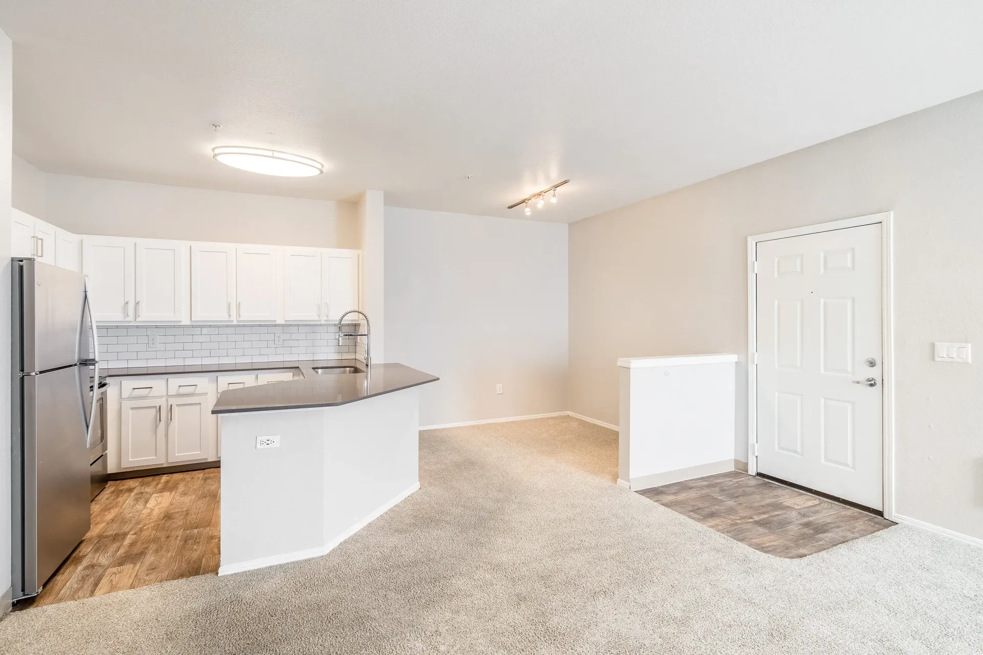 Open-concept kitchen with white cabinets, stainless steel fridge, island, and carpeted living area.