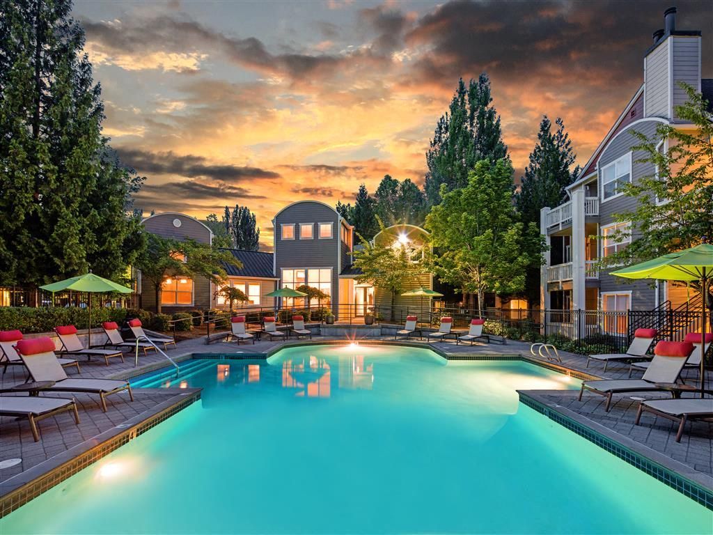 Outdoor community pool with lounge chairs and umbrellas at sunset.