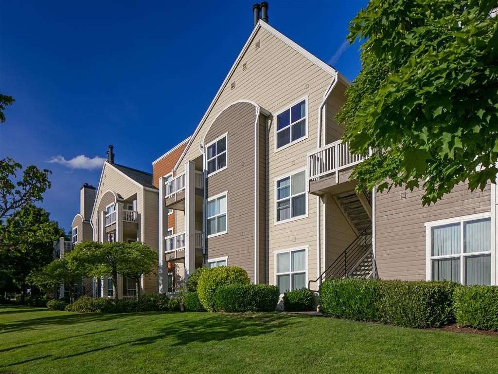 Exterior view of a beige multi-building apartment complex with balconies and lush green lawns.