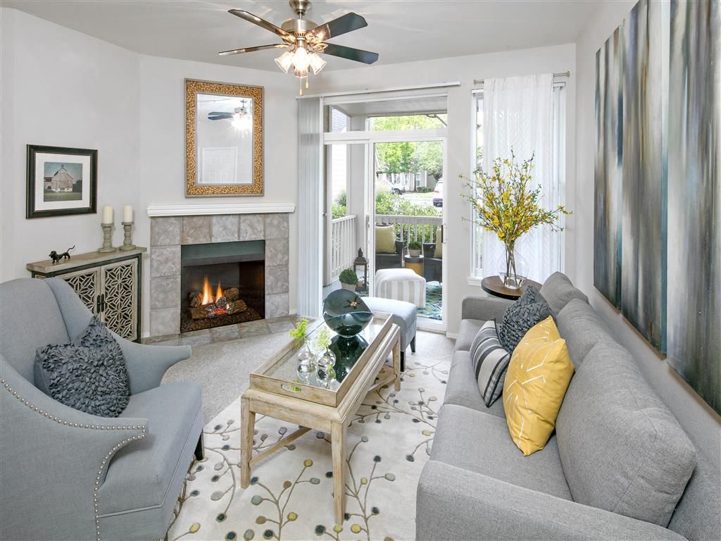 Living room with a gray sofa, light armchair, fireplace, and glass doors to a balcony.