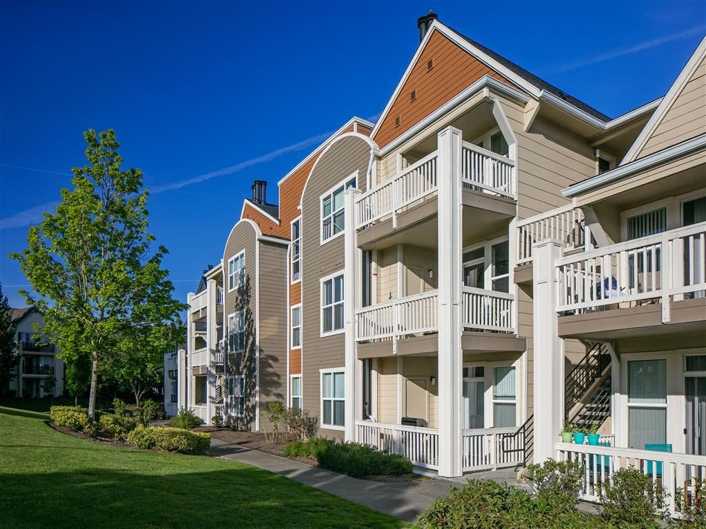 Exterior view of a multi-family apartment building with balconies and a landscaped lawn.