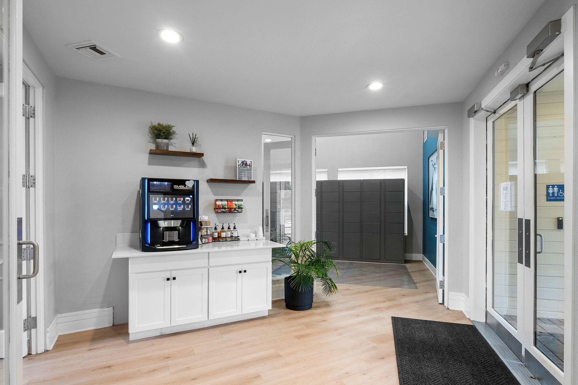 A bright, modern lobby with a coffee station, indoor plants, and double glass doors.