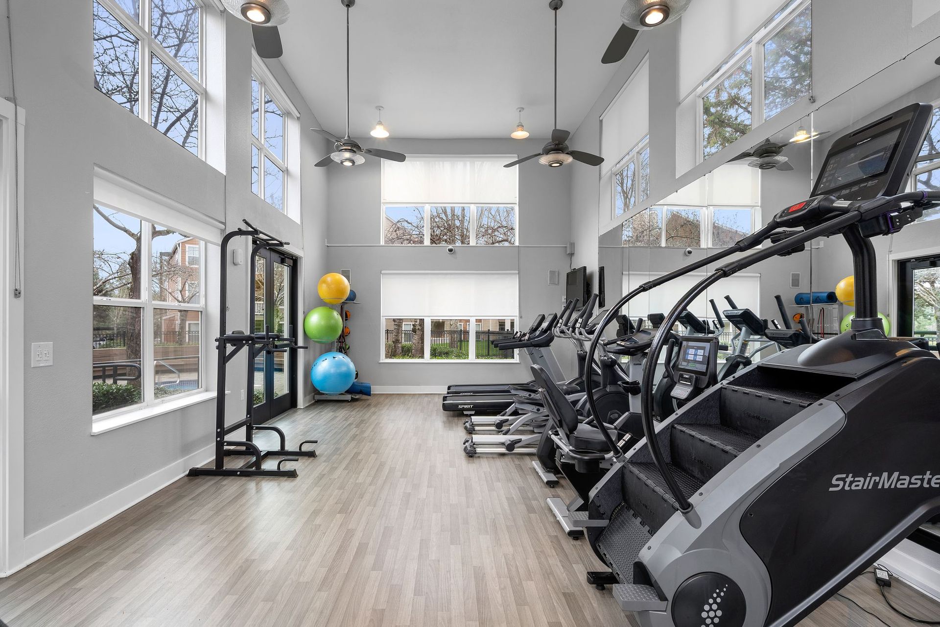 Gym interior with exercise equipment, high ceilings, large windows, and neutral colors.