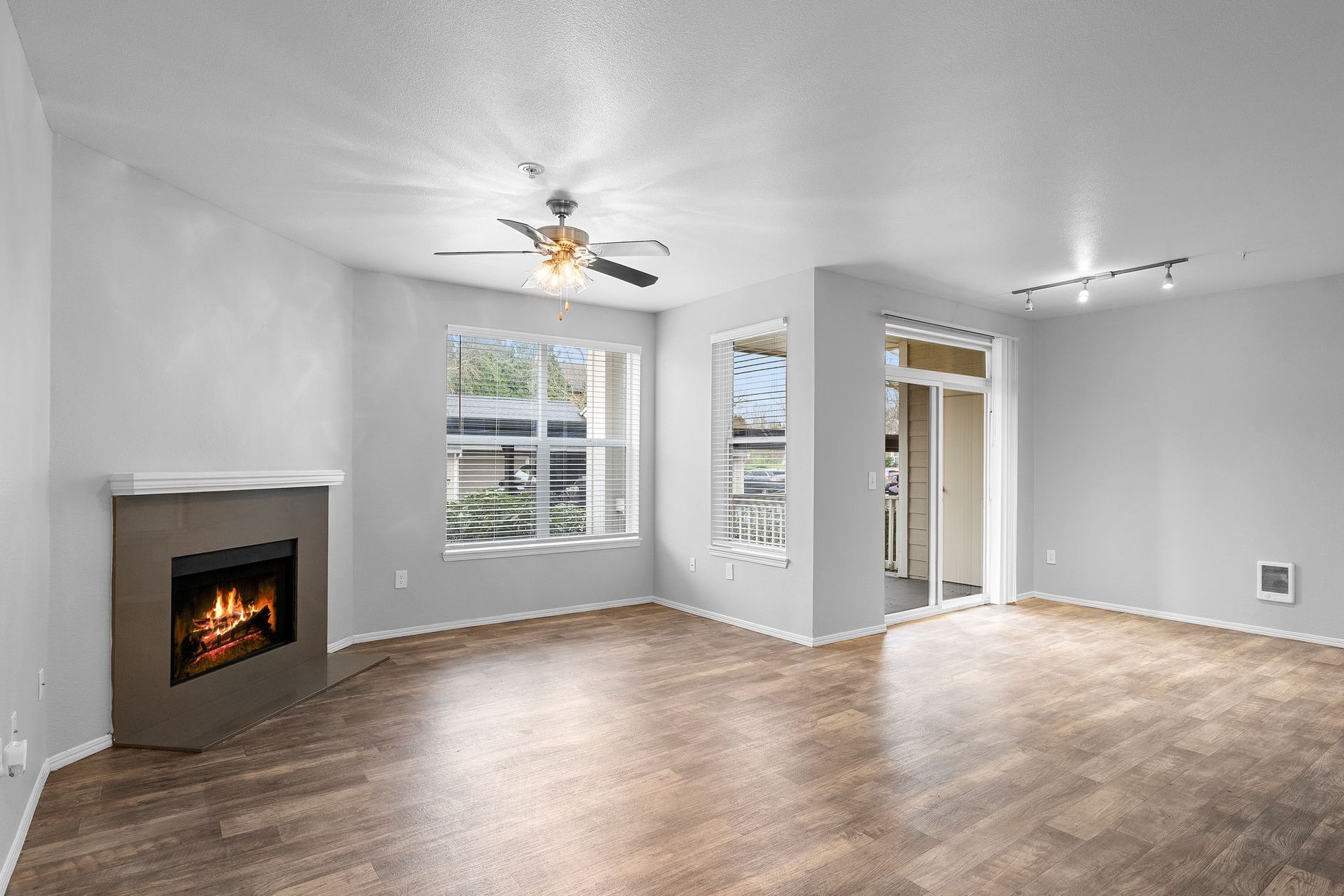 Empty living room with fireplace, window, and wood-look flooring.