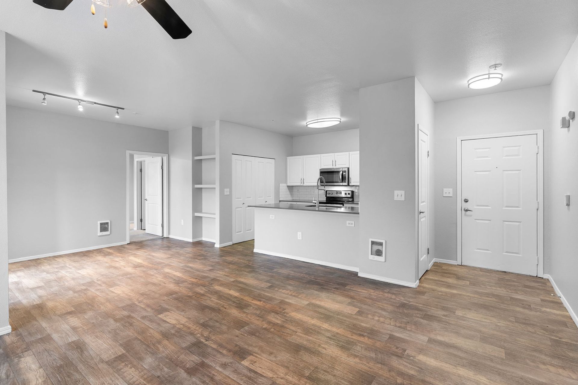 Empty apartment interior with wood-look flooring, white walls and cabinets, and built-in shelving.
