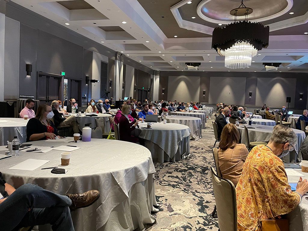 A large room filled with people sitting at tables with laptops.