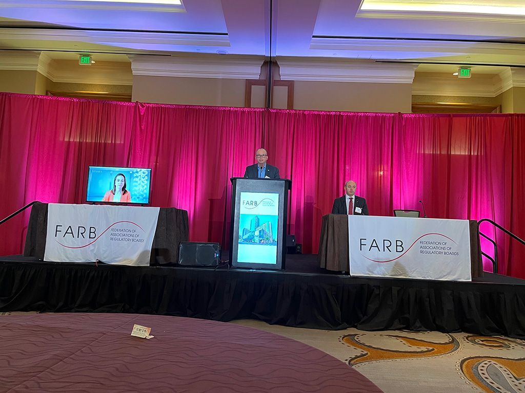 A man is standing at a podium in front of a pink curtain.