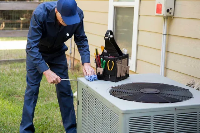 A man is working on an air conditioner outside of a house.