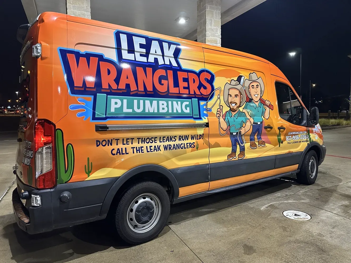 A leak wranglers plumbing van is parked in a gas station at night.