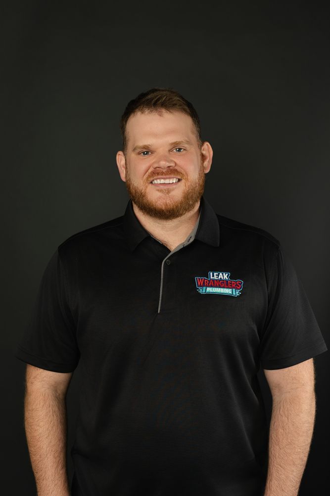 A man with a beard is wearing a black polo shirt and smiling.