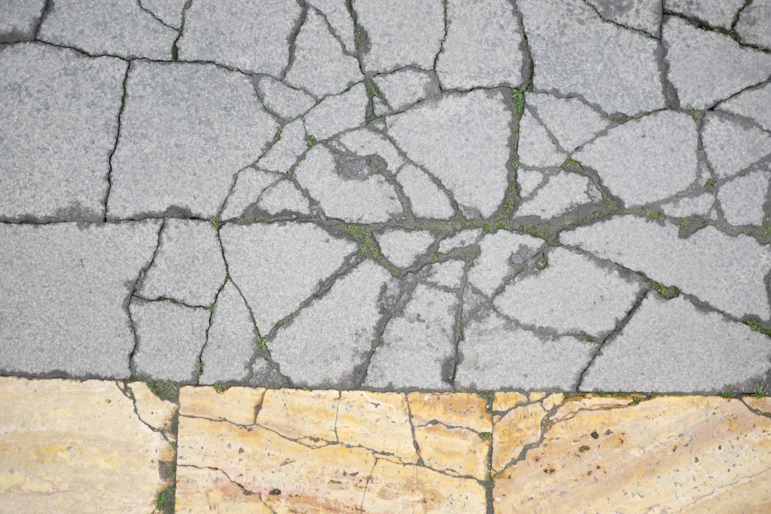 A close up of a cracked concrete floor with a yellow tile in the middle.