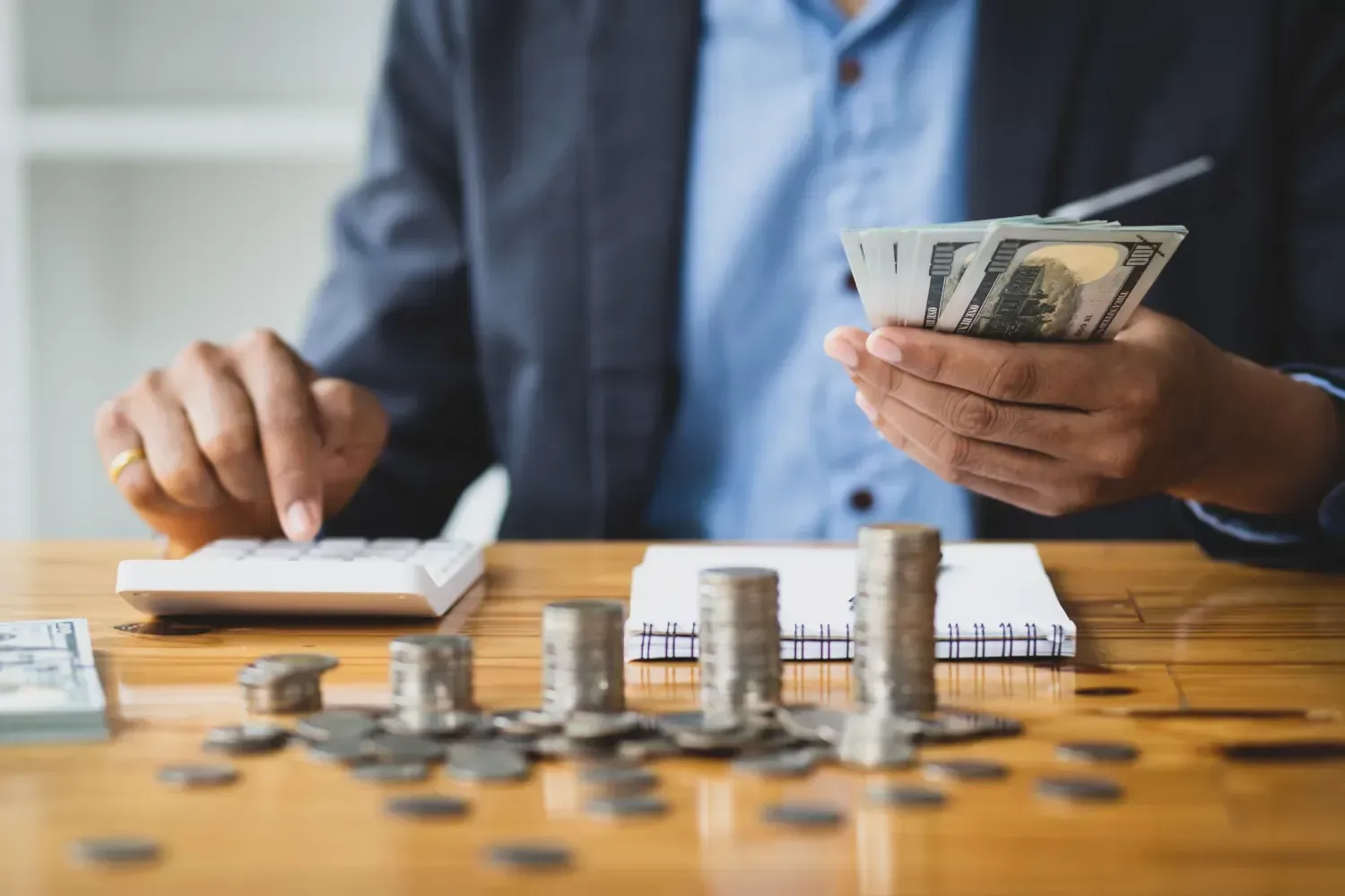 A man is sitting at a table holding money and a calculator.