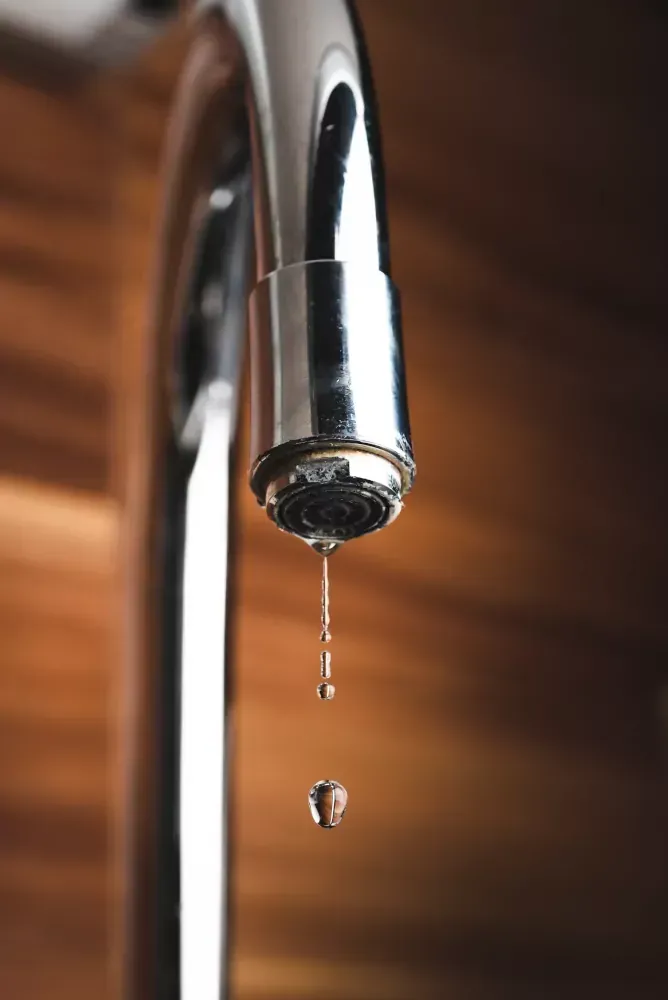 A close up of a faucet with a drop of water coming out of it.