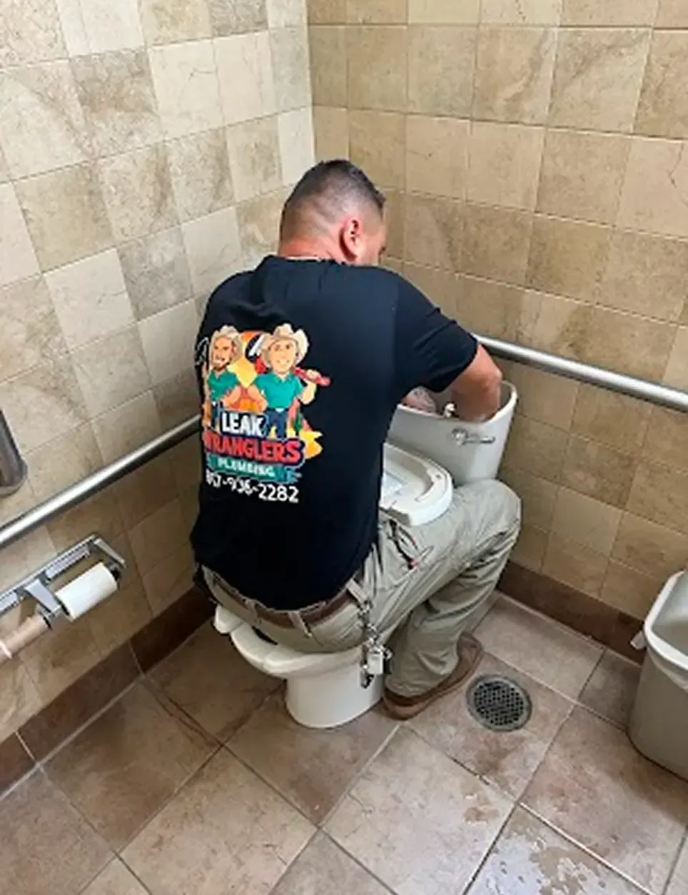 A man in a black shirt is fixing a toilet
