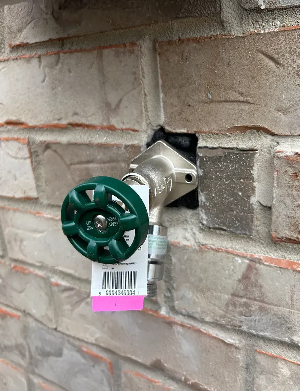 A green valve is attached to a brick wall.