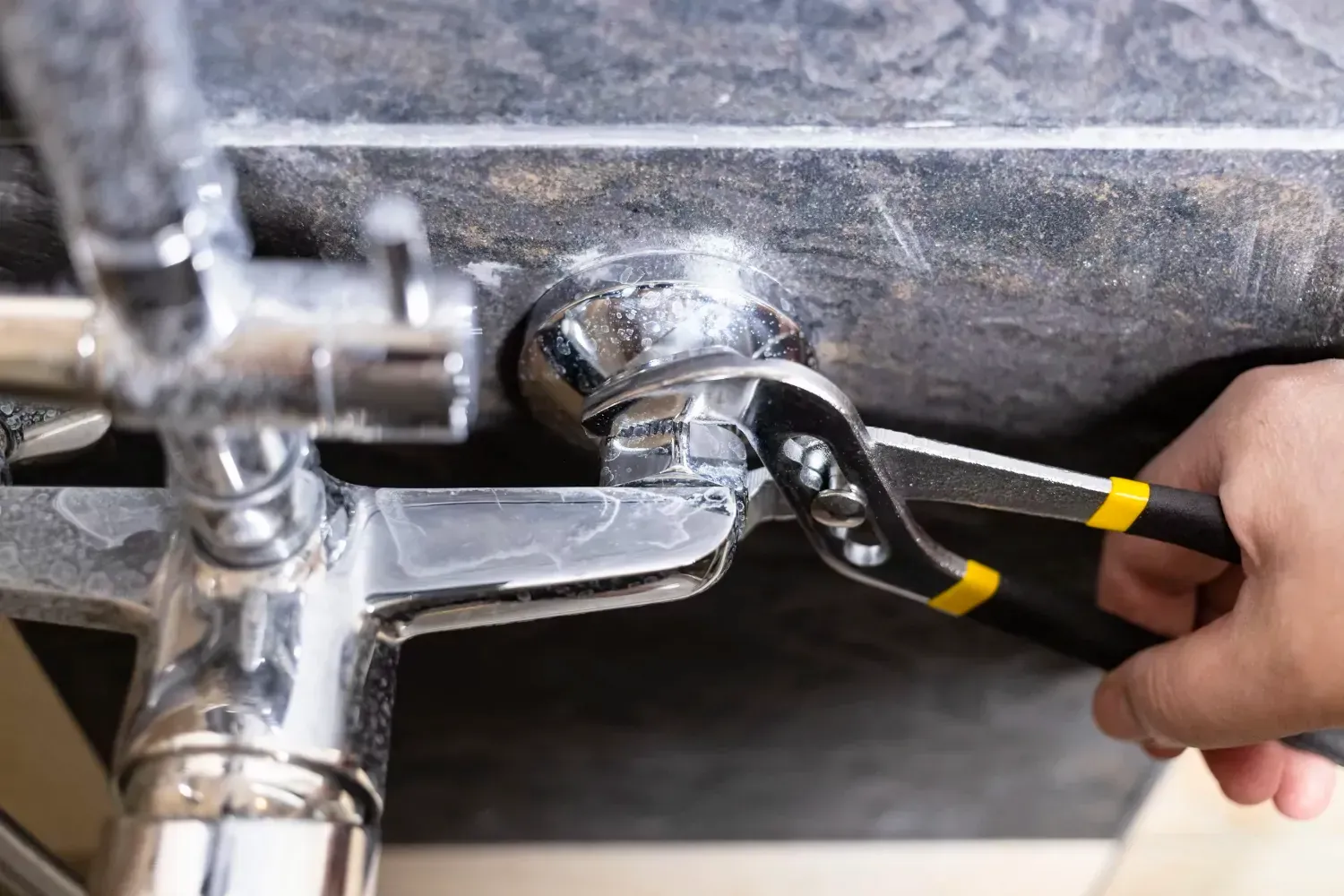 A person is fixing a faucet with a wrench.