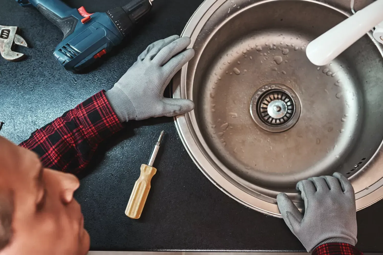 A man is fixing a kitchen sink with a screwdriver.