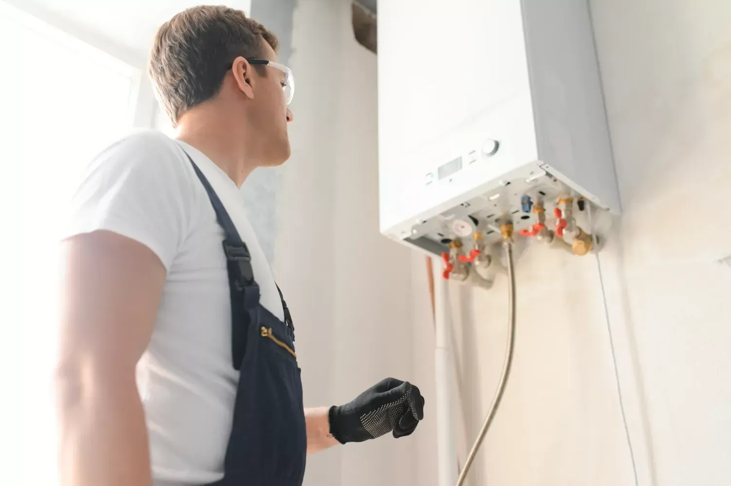 A man is looking at a boiler on the wall.