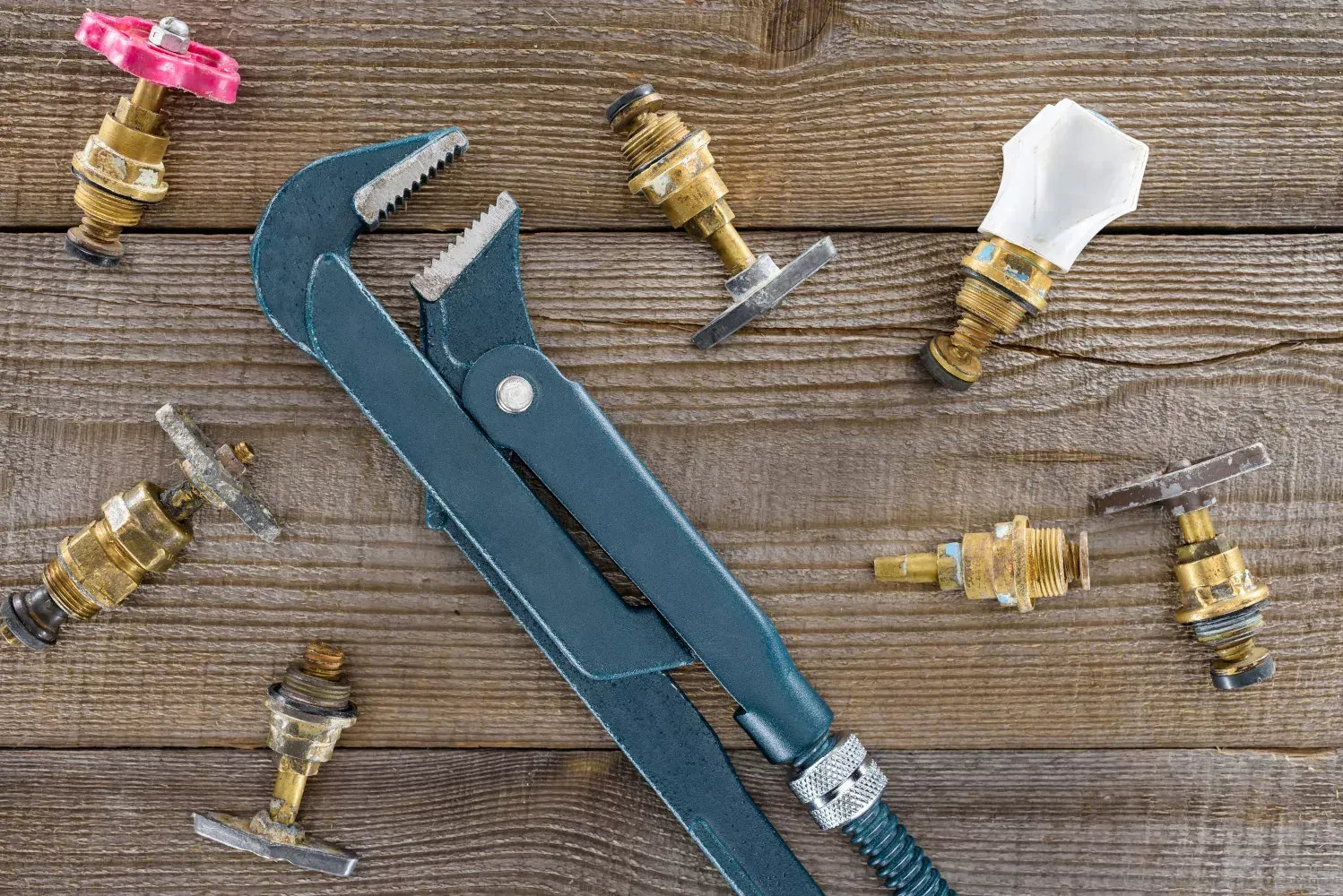 A wrench is sitting on top of a wooden table next to faucets and valves.