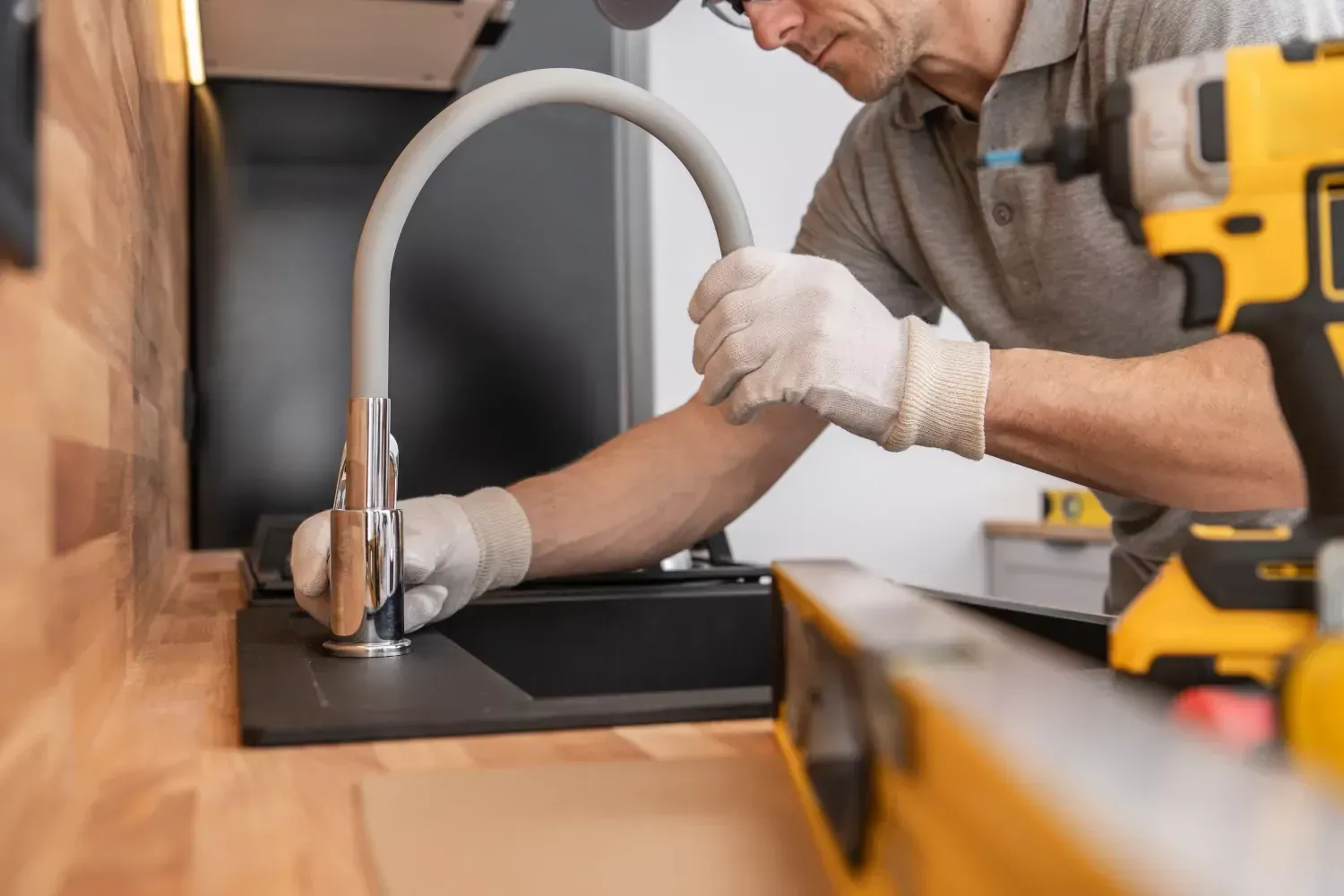 A man is fixing a sink with a drill and a level.