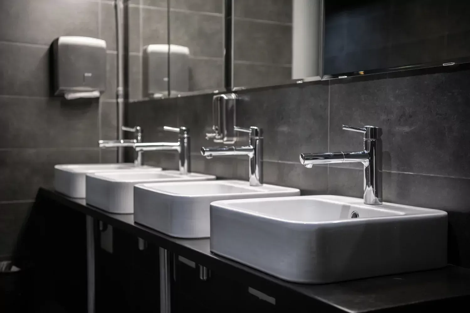 A bathroom with three sinks and a mirror.