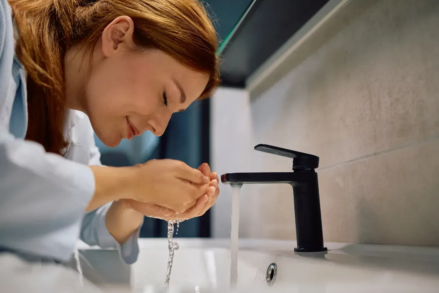 A woman is washing her face in a bathroom sink.