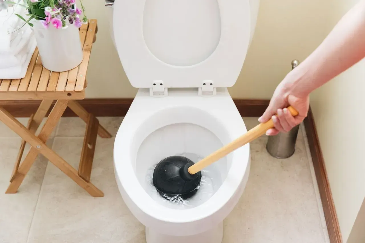 A person is using a plunger to unblock a toilet.