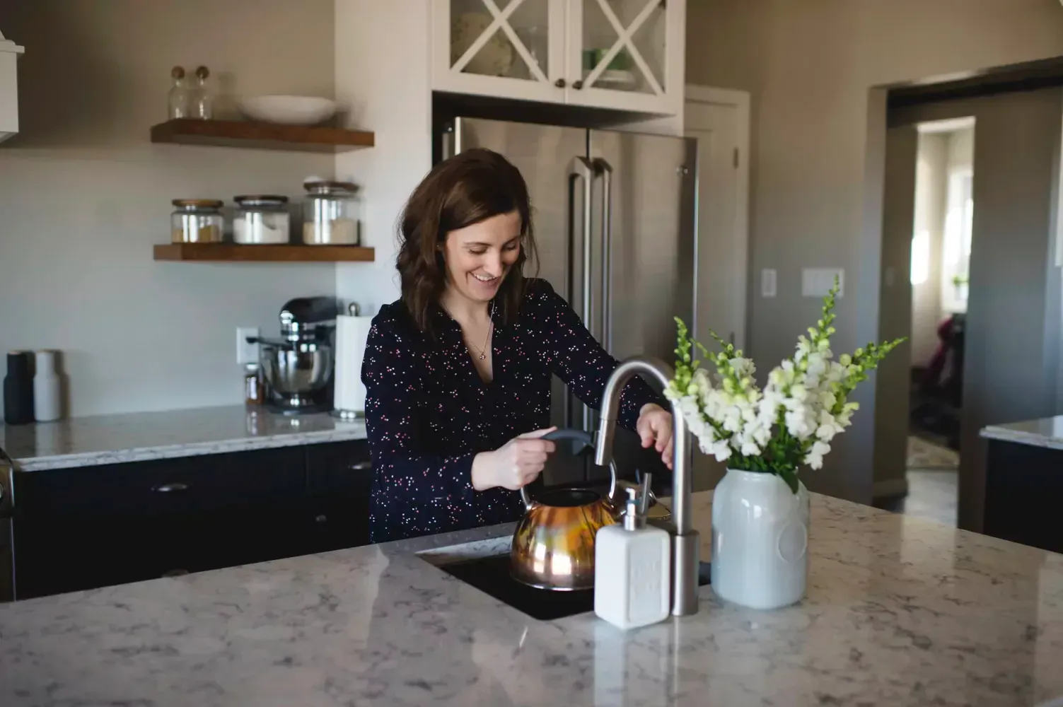 A woman is washing a tea kettle in a kitchen sink.