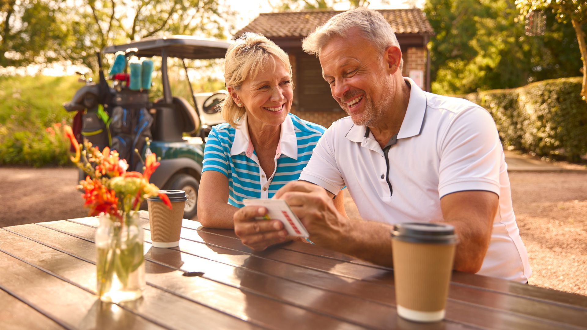 A man and a woman are sitting at a table looking at a cell phone.