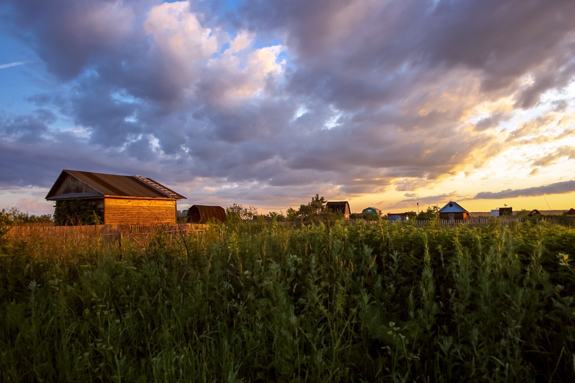 A small wooden house is sitting in the middle of a grassy field at sunset.