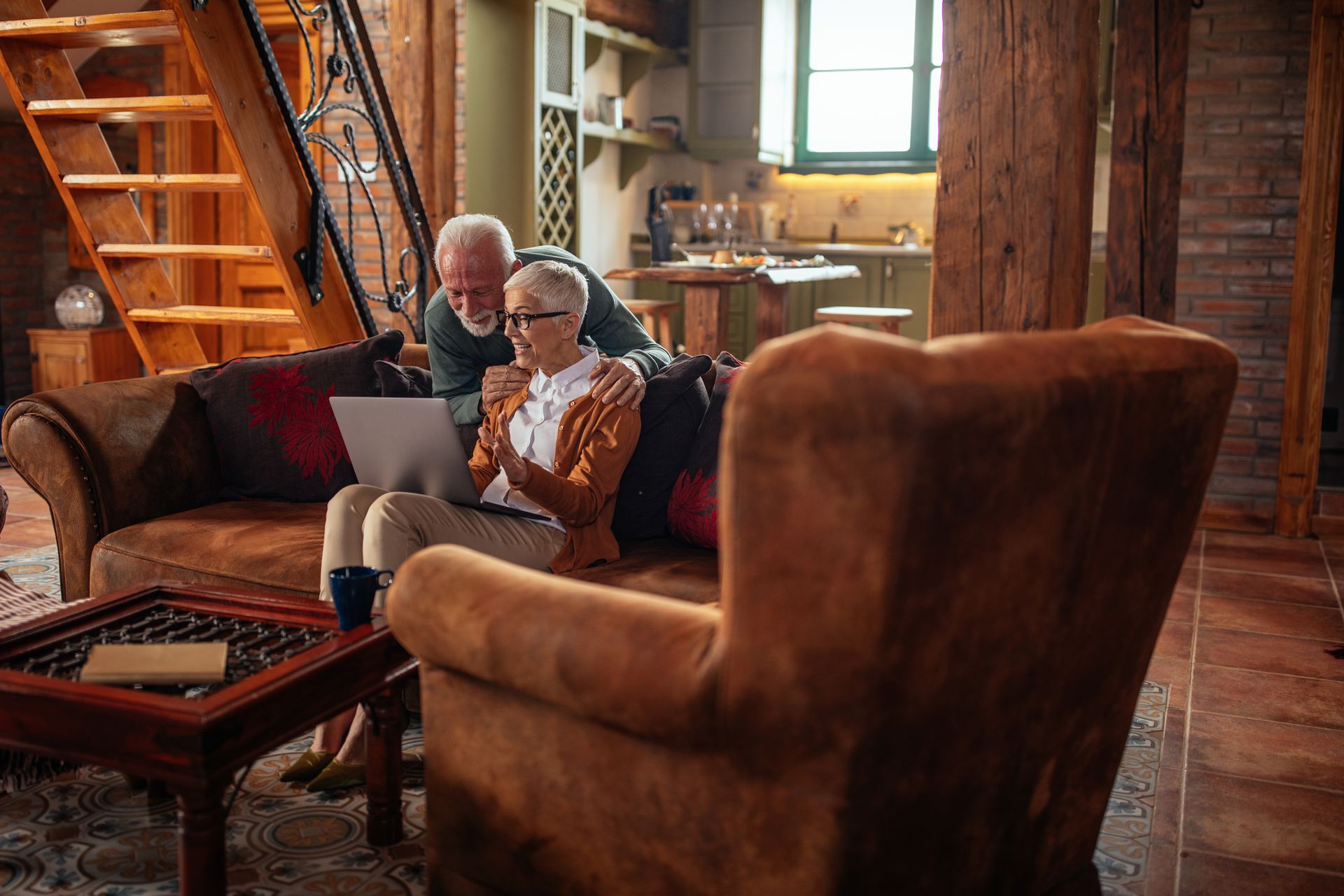 An elderly couple is sitting on a couch looking at a laptop.
