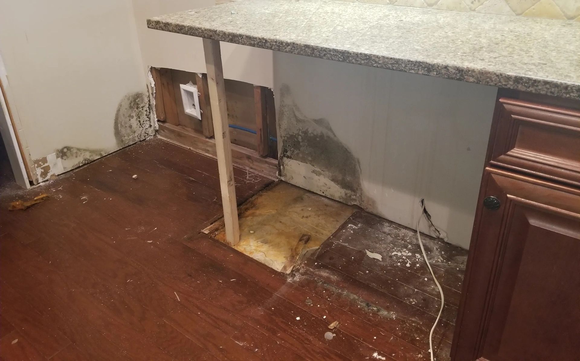 Kitchen with water damage, exposed wall, missing flooring, and countertop supported by a wooden beam.