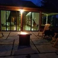 Night patio with a lit fire pit, glass doors, and lounge chairs under dim evening light