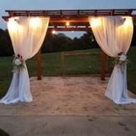 Draped white curtains and floral accents framing a wooden outdoor wedding arch at dusk