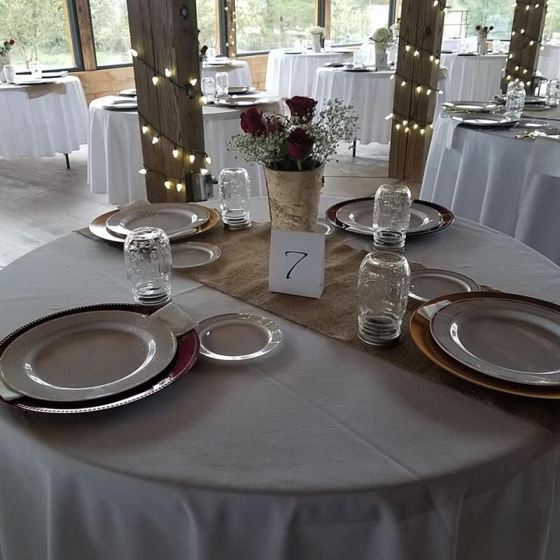 Round banquet table with white linens, glassware, and red napkins in a decorated event hall, table 7.