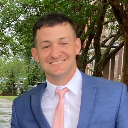 A man in a blue suit and pink tie is smiling for the camera.
