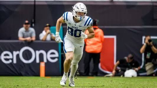 Football player in white and blue jersey running on the field with a dark stadium backdrop