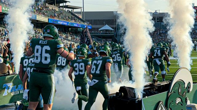 A group of football players are running on a field with smoke coming out of the tunnel.