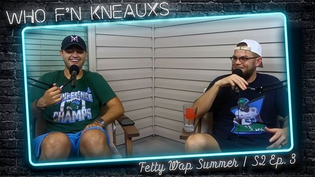 Two men are sitting in front of a brick wall and talking into microphones.