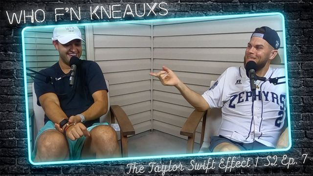 Two men are sitting in front of a brick wall and talking into microphones.