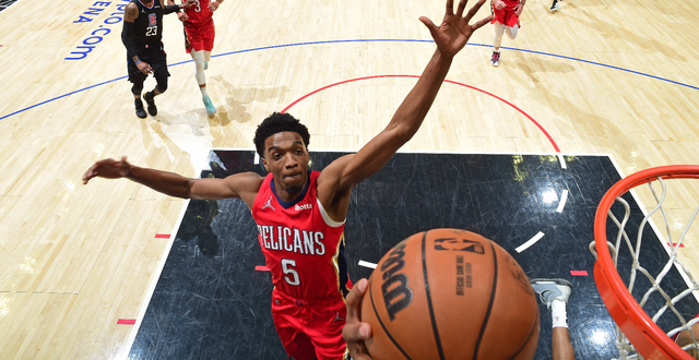 A basketball player wearing a red jersey with the number 5 on it is going for the ball.