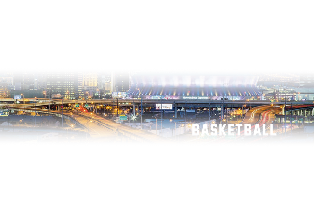 A basketball stadium in the middle of a city at night.