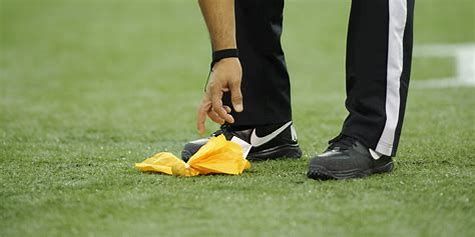 A referee is standing on a football field with a yellow flag on the ground.