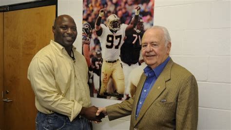 Two men shaking hands in front of a picture of a football player wearing number 97