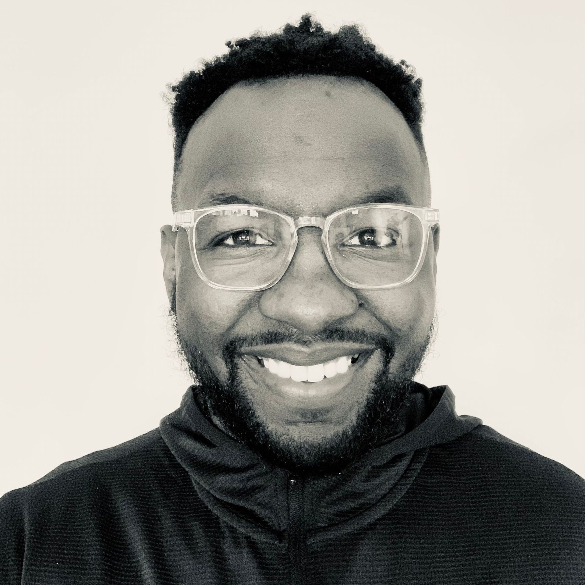 A man with glasses and a beard is smiling in a black and white photo.